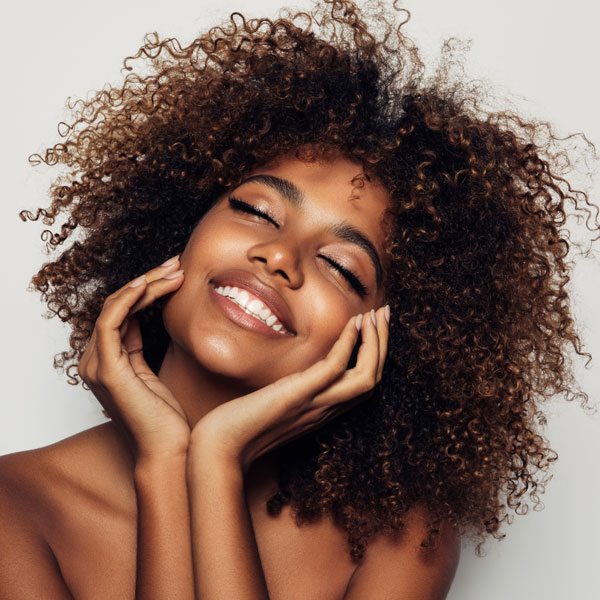 woman smiling with eyes closed and both hands touching the sides of her face